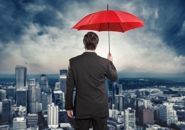 Man in a suit holding a red umbrella above a city skyline under a cloudy sky