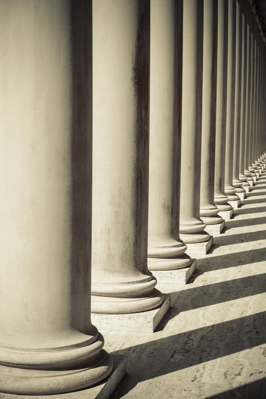 Row of white columns casting long diagonal shadows in sunlight