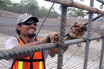 Construction worker in orange safety vest and hard hat tying rebar at a job site