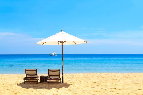 Two beach chairs under a white umbrella on a sunny sandy beach with blue ocean and sky