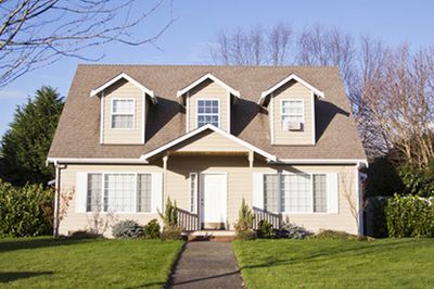 Suburban house with beige siding, brown roof, and a front walkway bordered by green lawn.