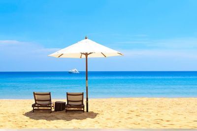 Two lounge chairs under a white umbrella on a sunny beach with blue sea and sky