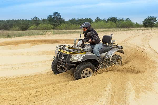 ATV rider turns through a sandy dirt track, kicking up dust in an open field.