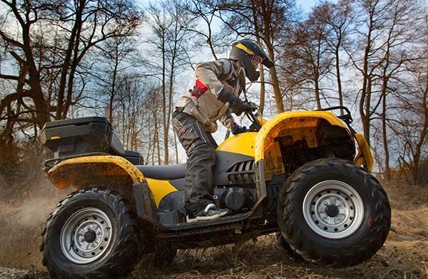 Person riding a yellow ATV through muddy terrain in a wooded area