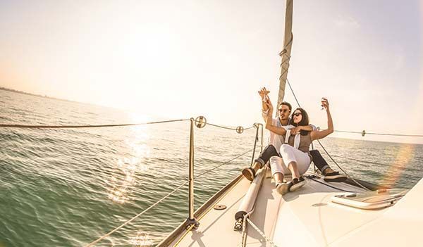 Two people relaxing on a sailboat deck at sunset, with calm water and a warm sky