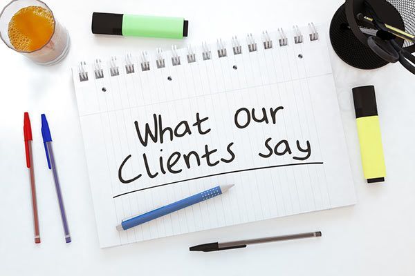 Notebook page reading “What our Clients say” with pens, highlighter, and coffee on a desk