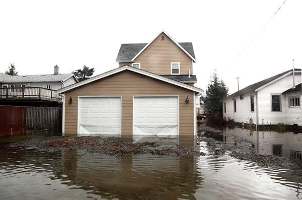 Flooded driveway with a beige garage and house, water covering the street and yard