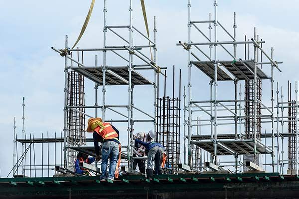 Construction workers on scaffolding at a building site, wearing safety vests and helmets.