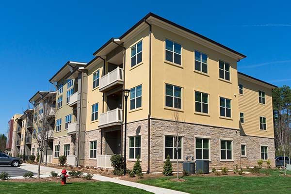 Modern beige apartment building with balconies, stone accents, and green lawn under a blue sky