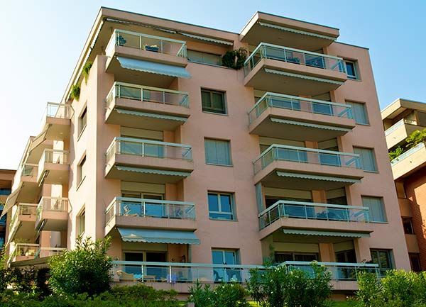 Modern apartment building with balconies and a pink facade, viewed from below against a blue sky