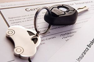 Two car keys on an insurance document, one black and one white key fob