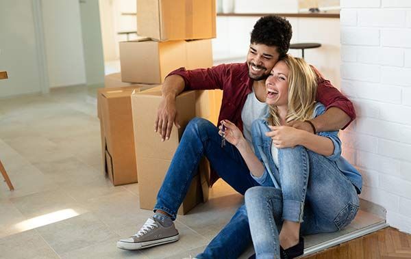 Two people sitting on a floor by moving boxes, smiling and relaxing in a bright room