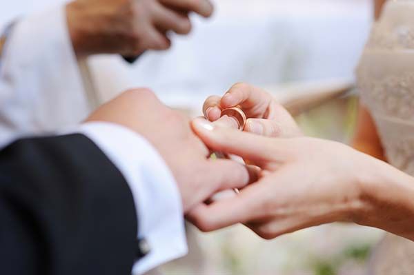 Hands exchanging wedding rings during a ceremony, with blurred guests in the background