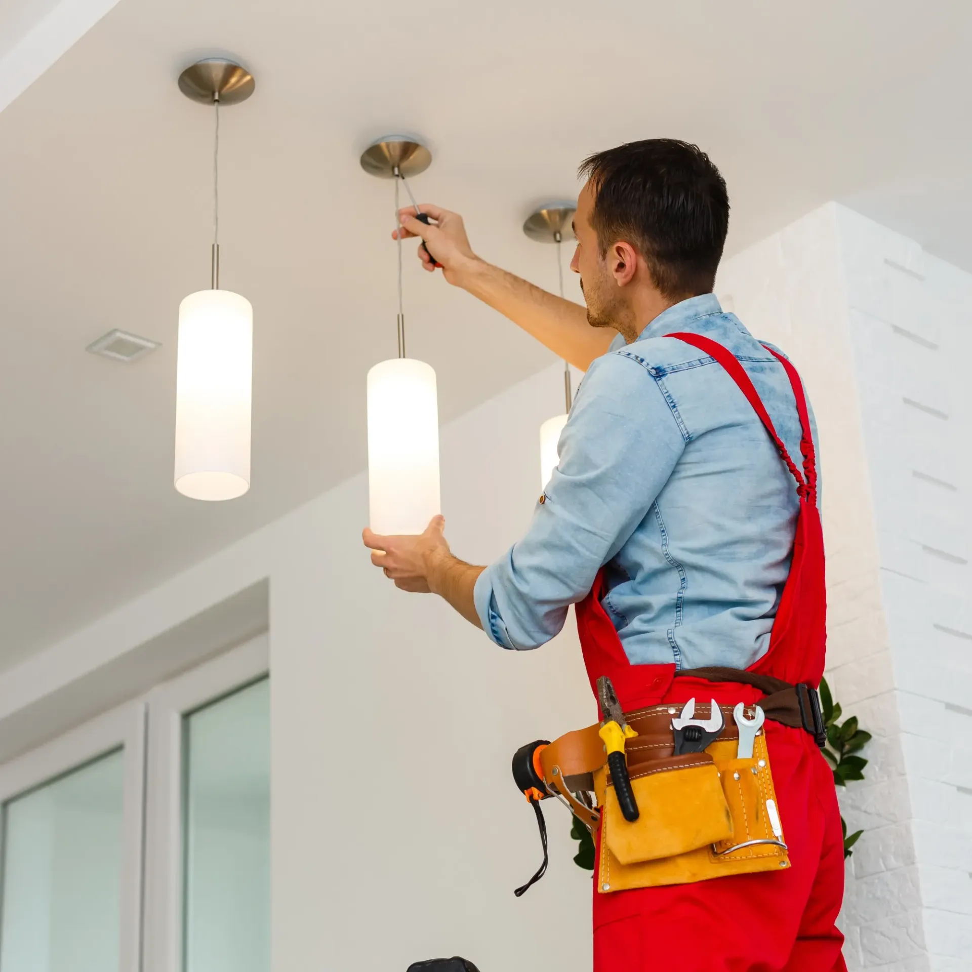 Sanchez Electric and Remodeling - A man in red overalls is hanging a light from the ceiling.
