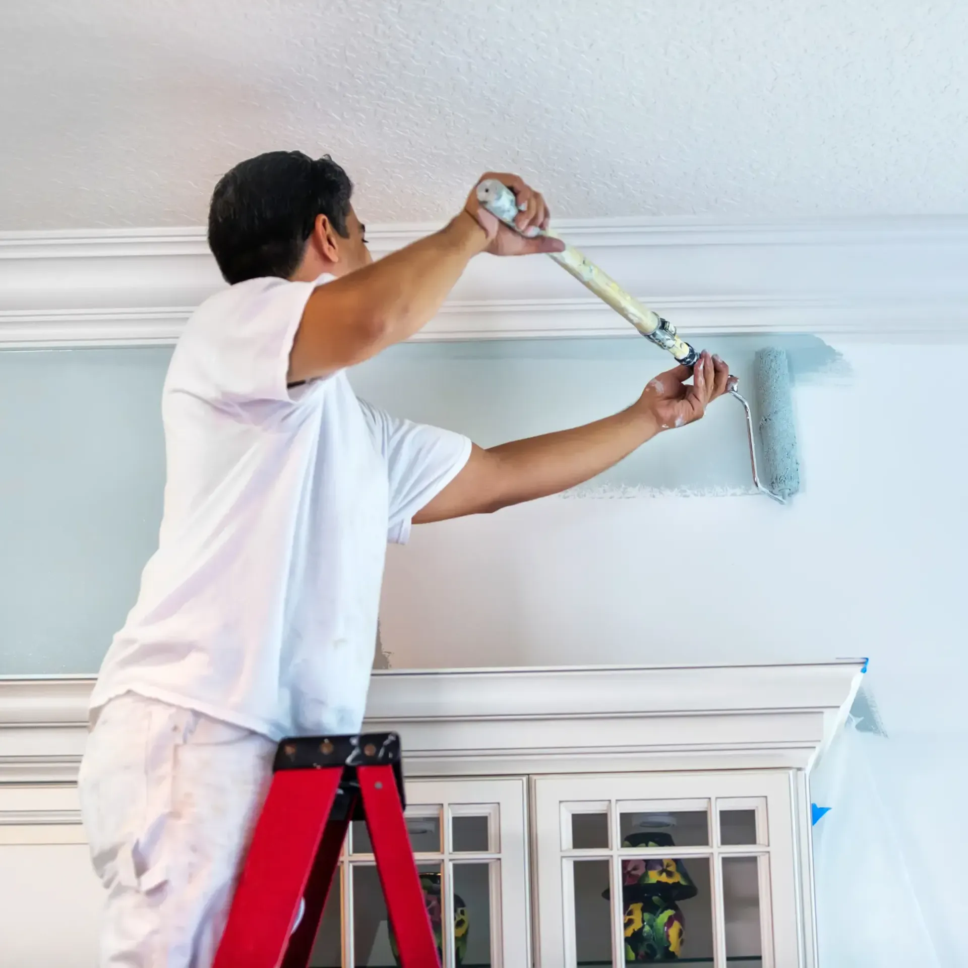 Sanchez Electric and Remodeling - A man is standing on a ladder painting a wall