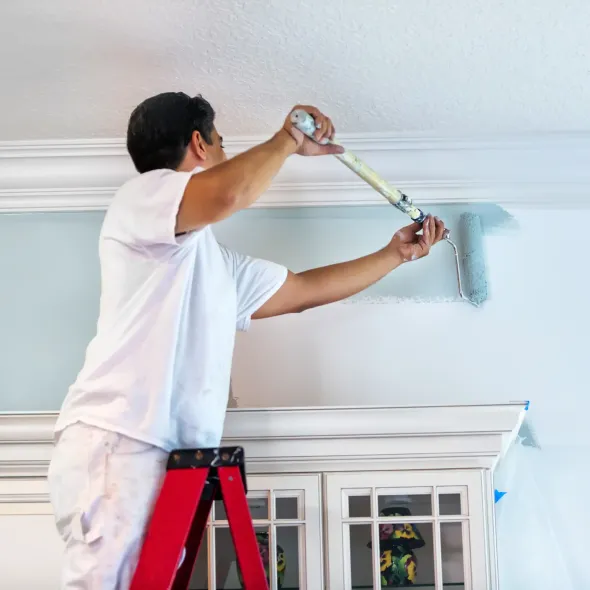 Sanchez Electric and Remodeling - A man is standing on a ladder painting a wall