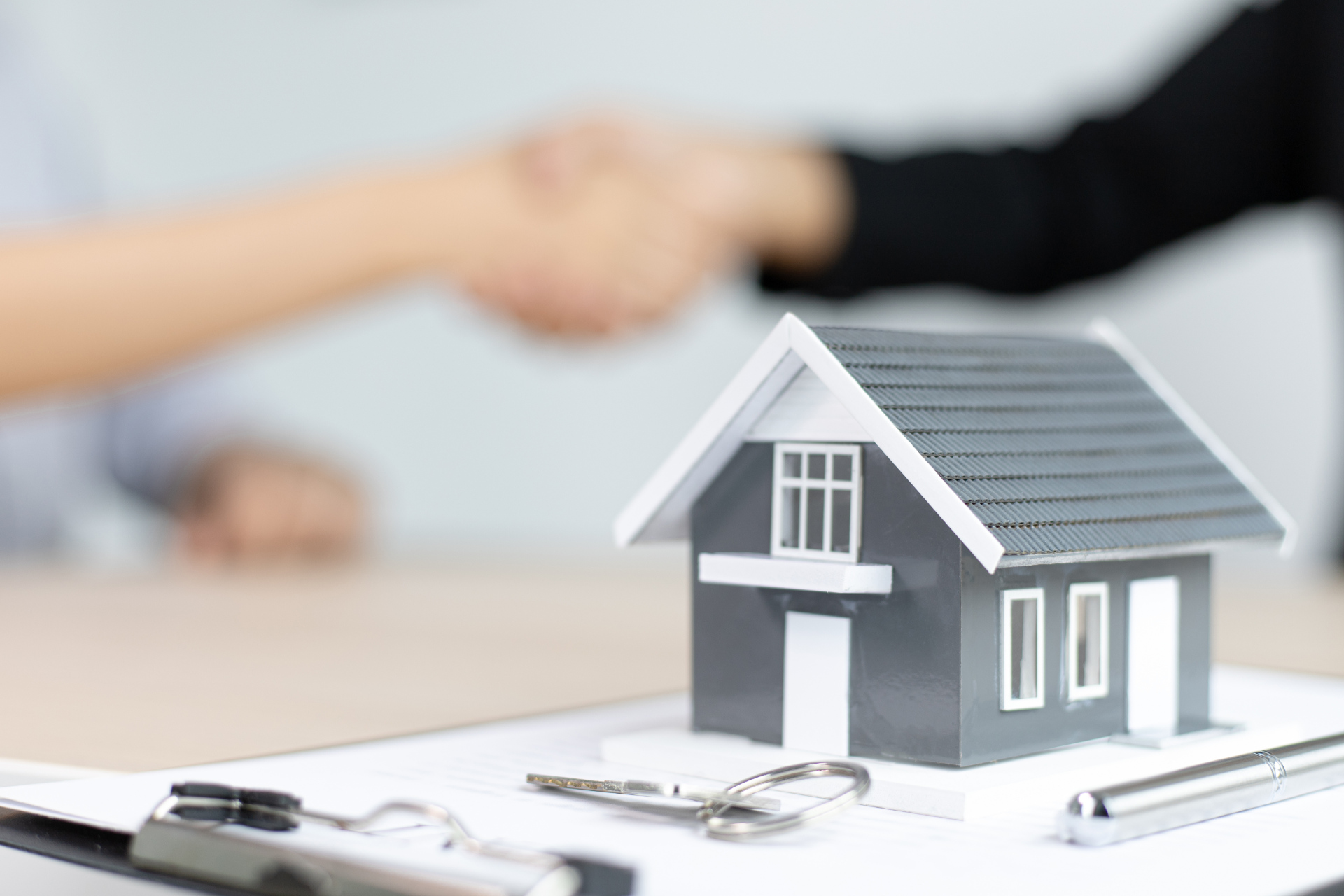 Hand shaking over a model house on a desk, with keys in the foreground