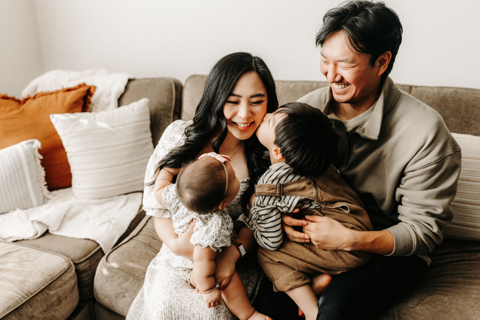 Family sitting on a couch, smiling and holding two babies in a cozy living room