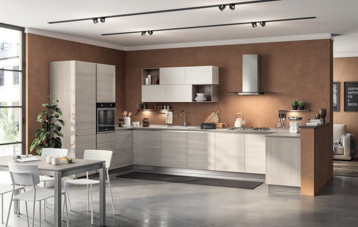 Cucina moderna con mobili in legno chiaro, pensili bianco opaco, cappa in acciaio inox e pareti color marrone caldo.