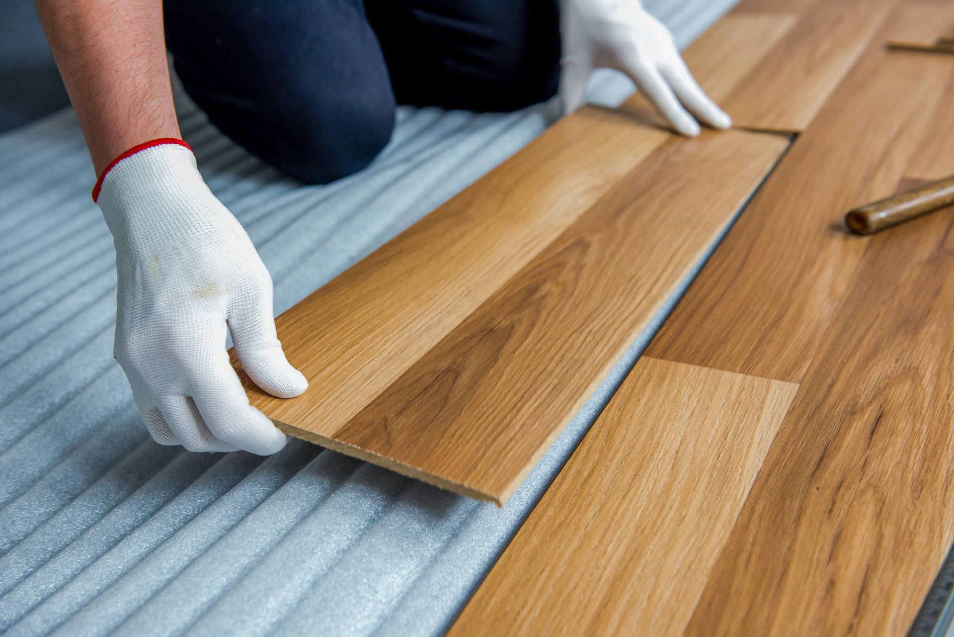 Hands in white gloves installing wooden floorboards
