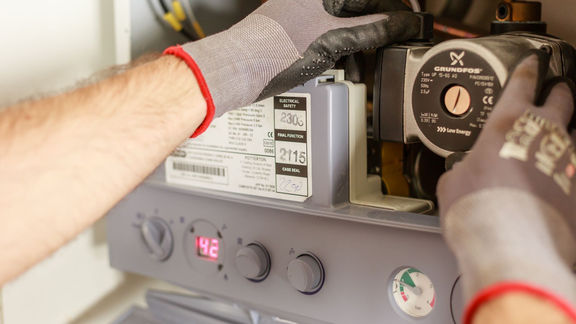 Person in gloves fixing a boiler, dials at 42 degrees.