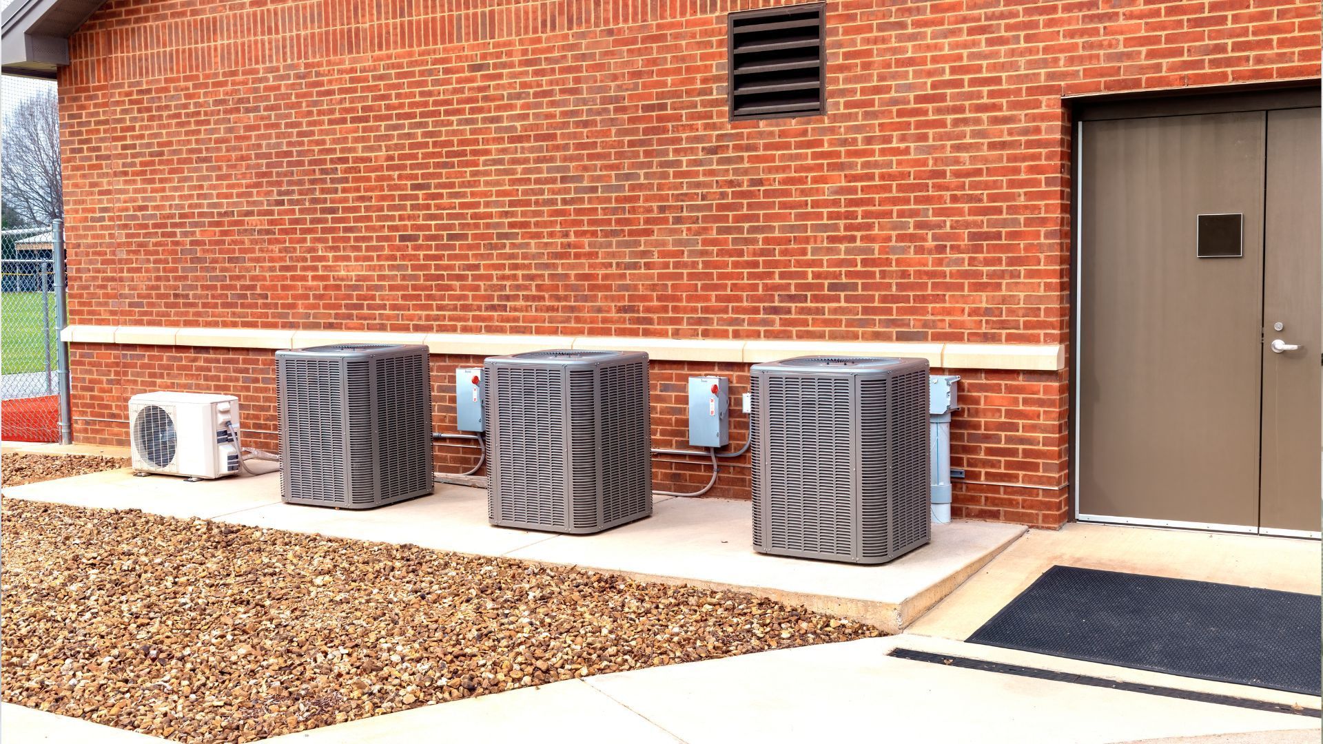 Brick building exterior with air conditioning units, door, and landscaping.