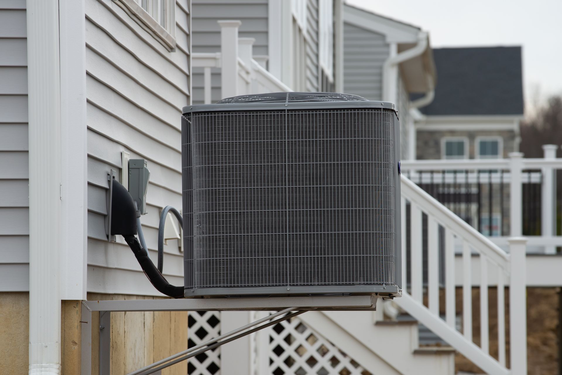 Air conditioning unit outside a house with gray siding and a white staircase.