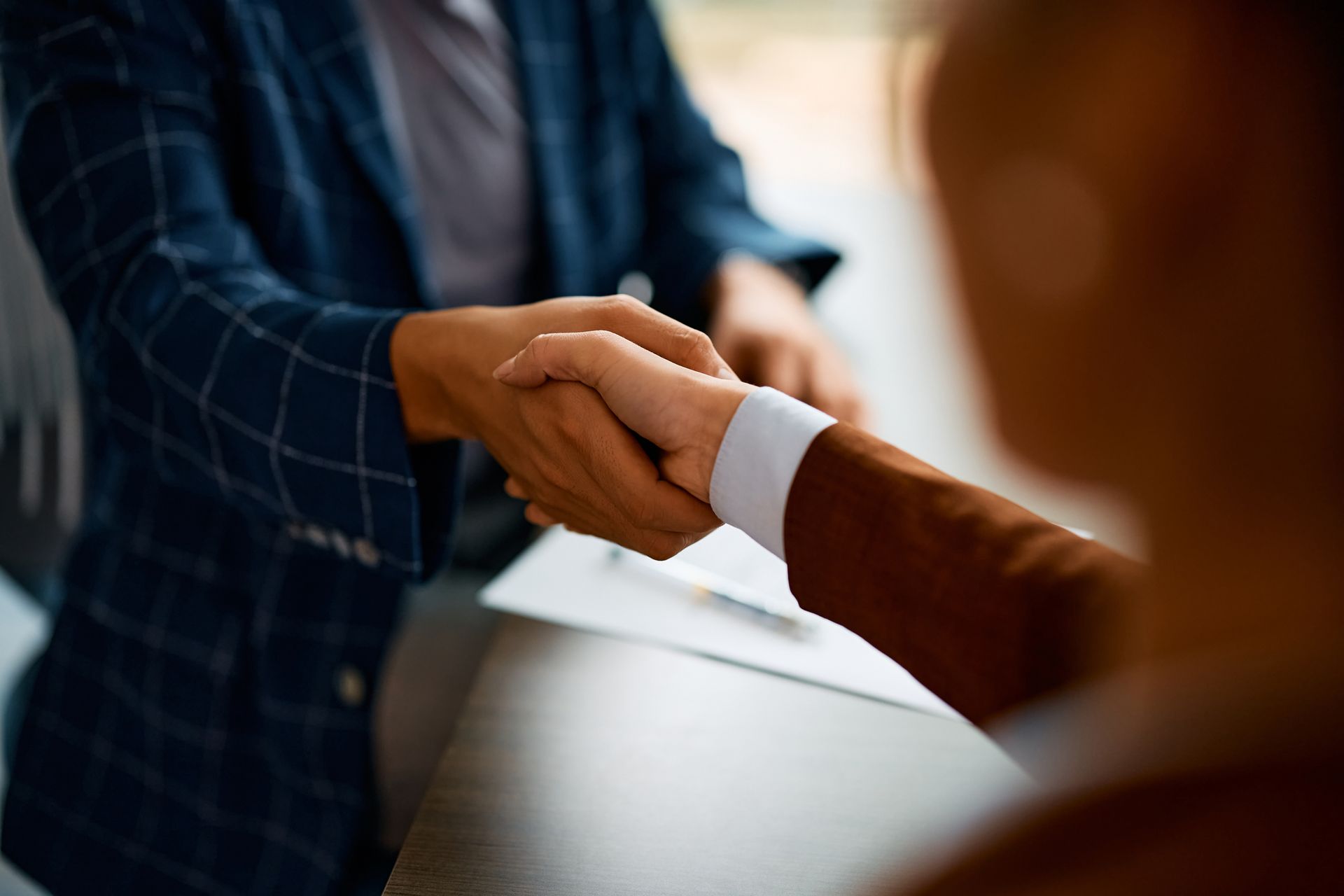 Two people in business attire shaking hands across a desk, signifying agreement.