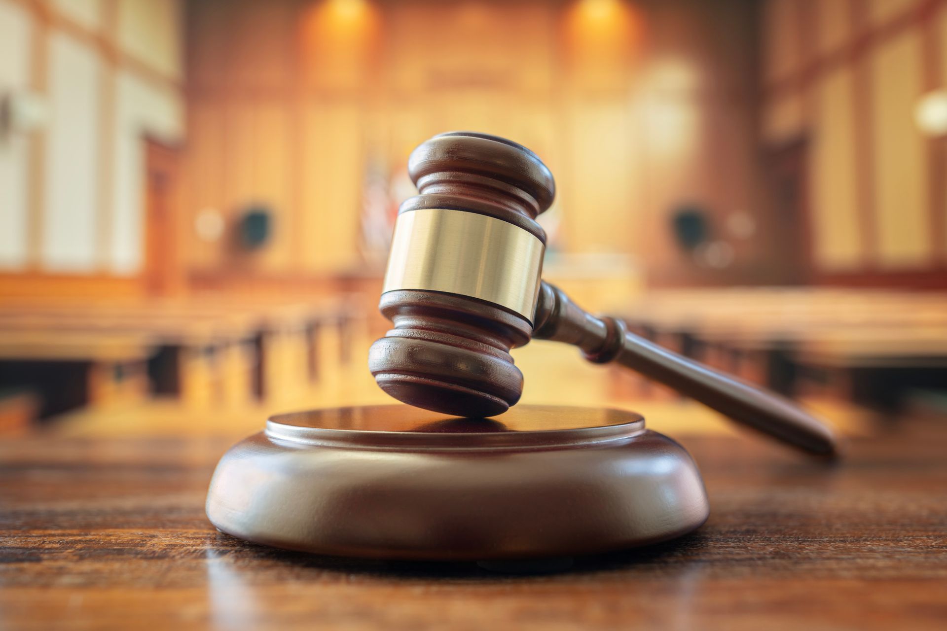 Gavel on a wooden block in a courtroom setting, with a blurred background of seats and wood paneling.