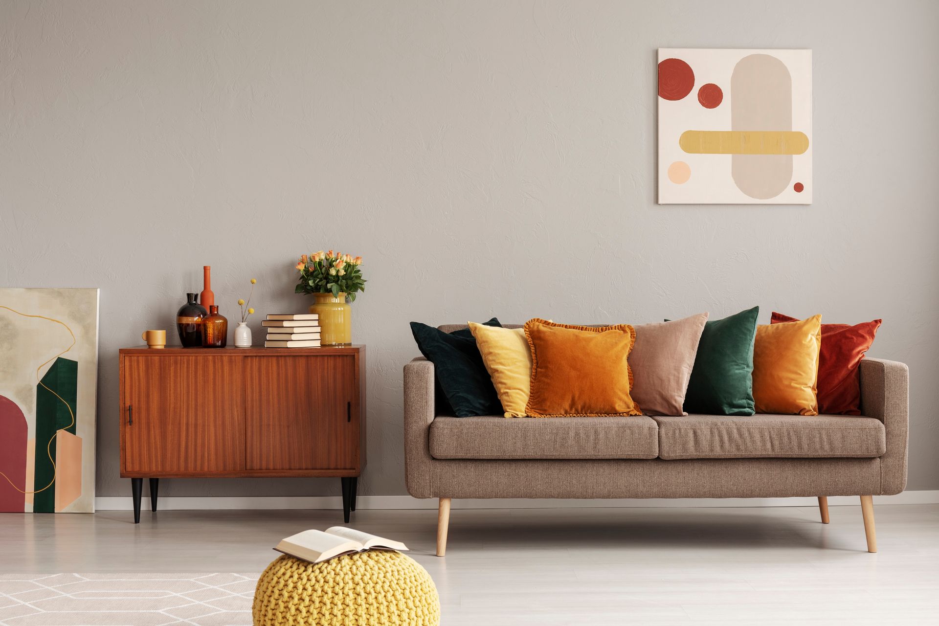 A living room with a couch , ottoman , and painting on the wall.