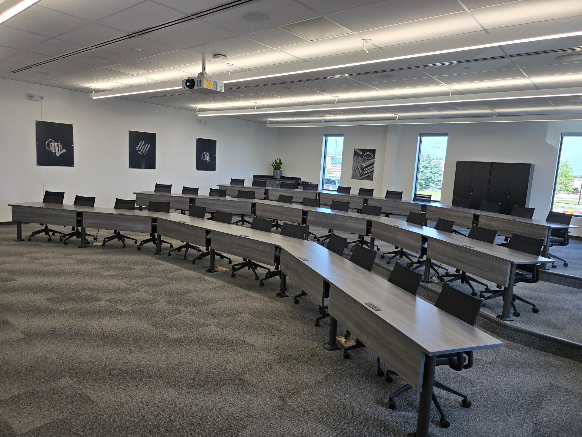 Empty modern classroom with curved desks, black chairs, carpeted floor, and wall-mounted displays.