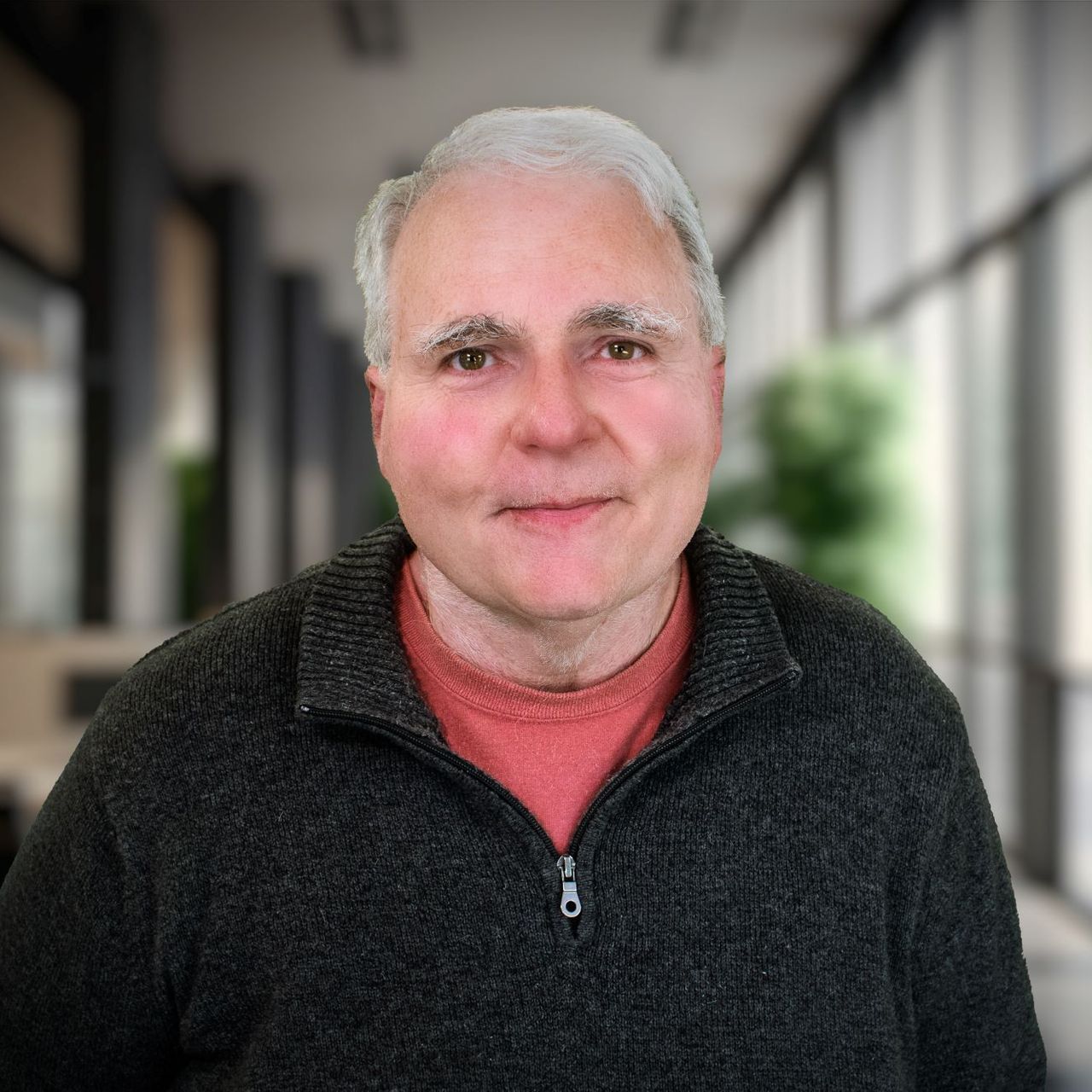 A man wearing a black sweater and a red shirt is standing in a hallway.