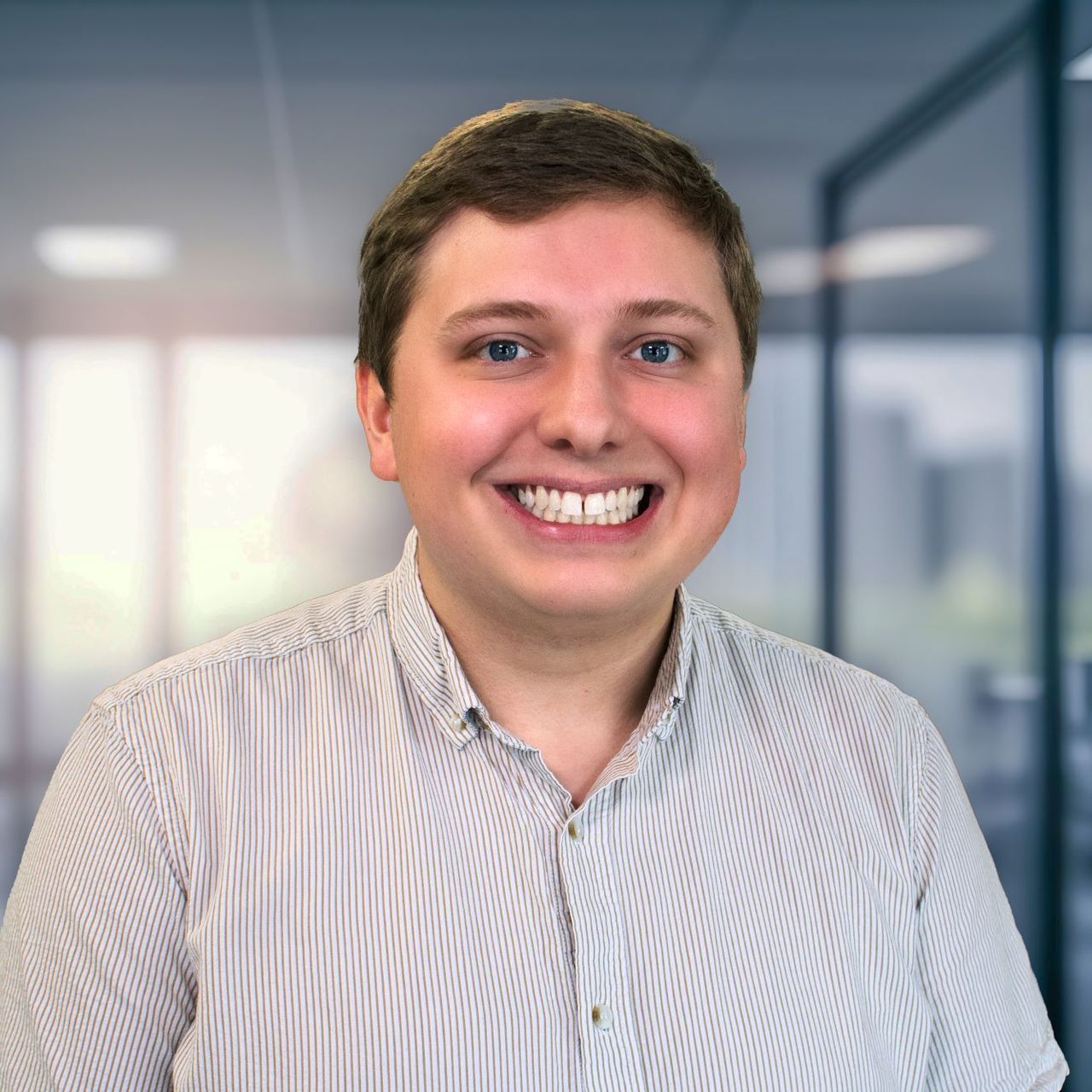A man in a striped shirt is smiling for the camera in an office.