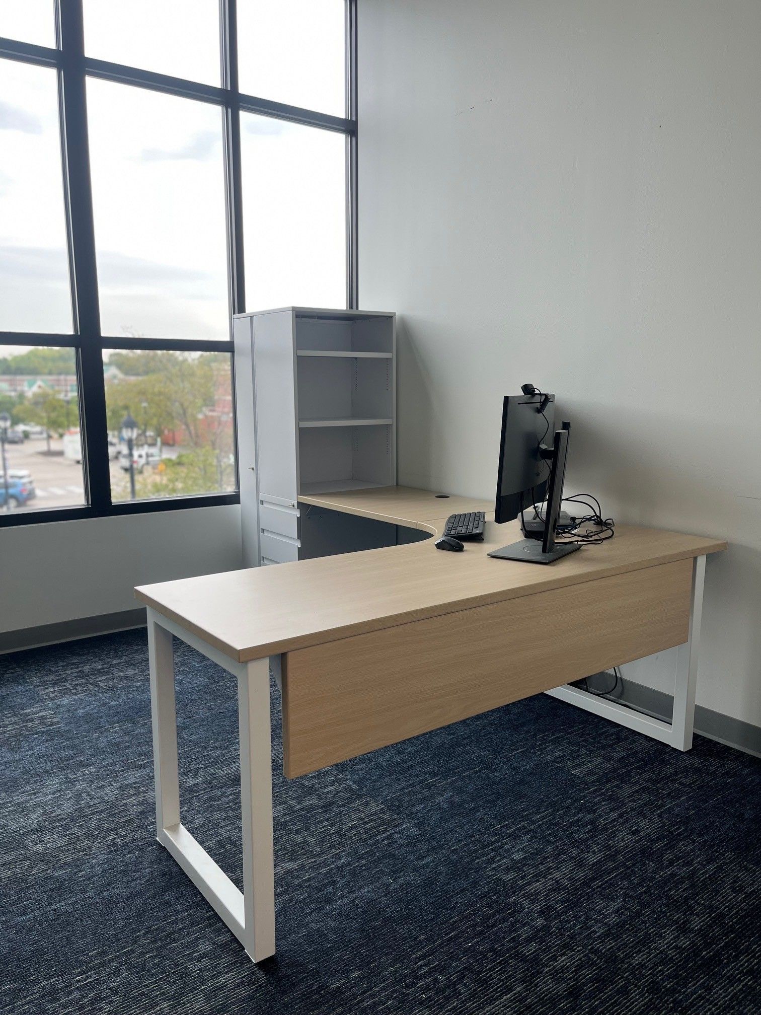 Empty modern office with desk, monitor, shelving, and large window.