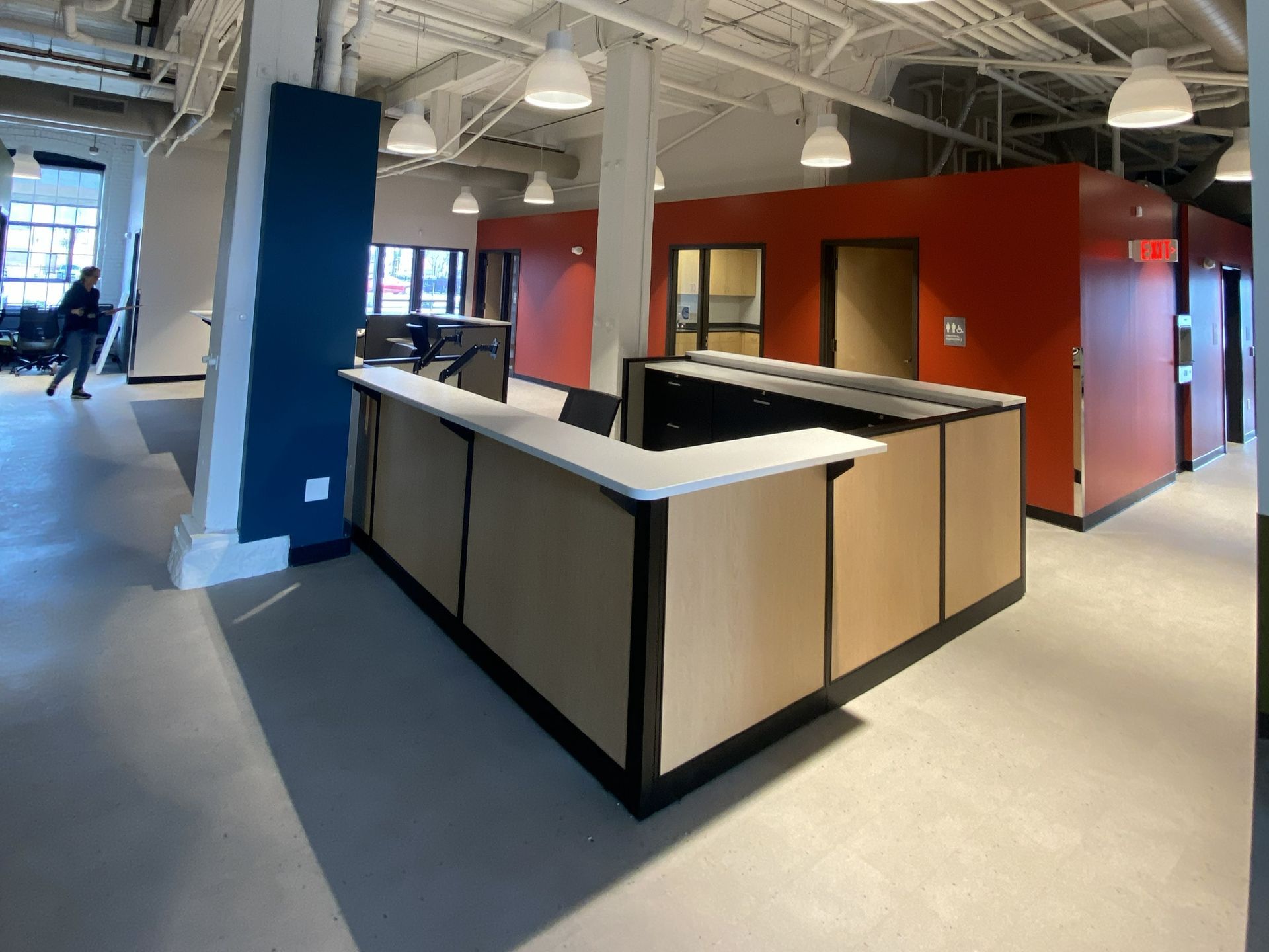 Modern office interior with a central work counter, red partition walls, and exposed ceiling beams