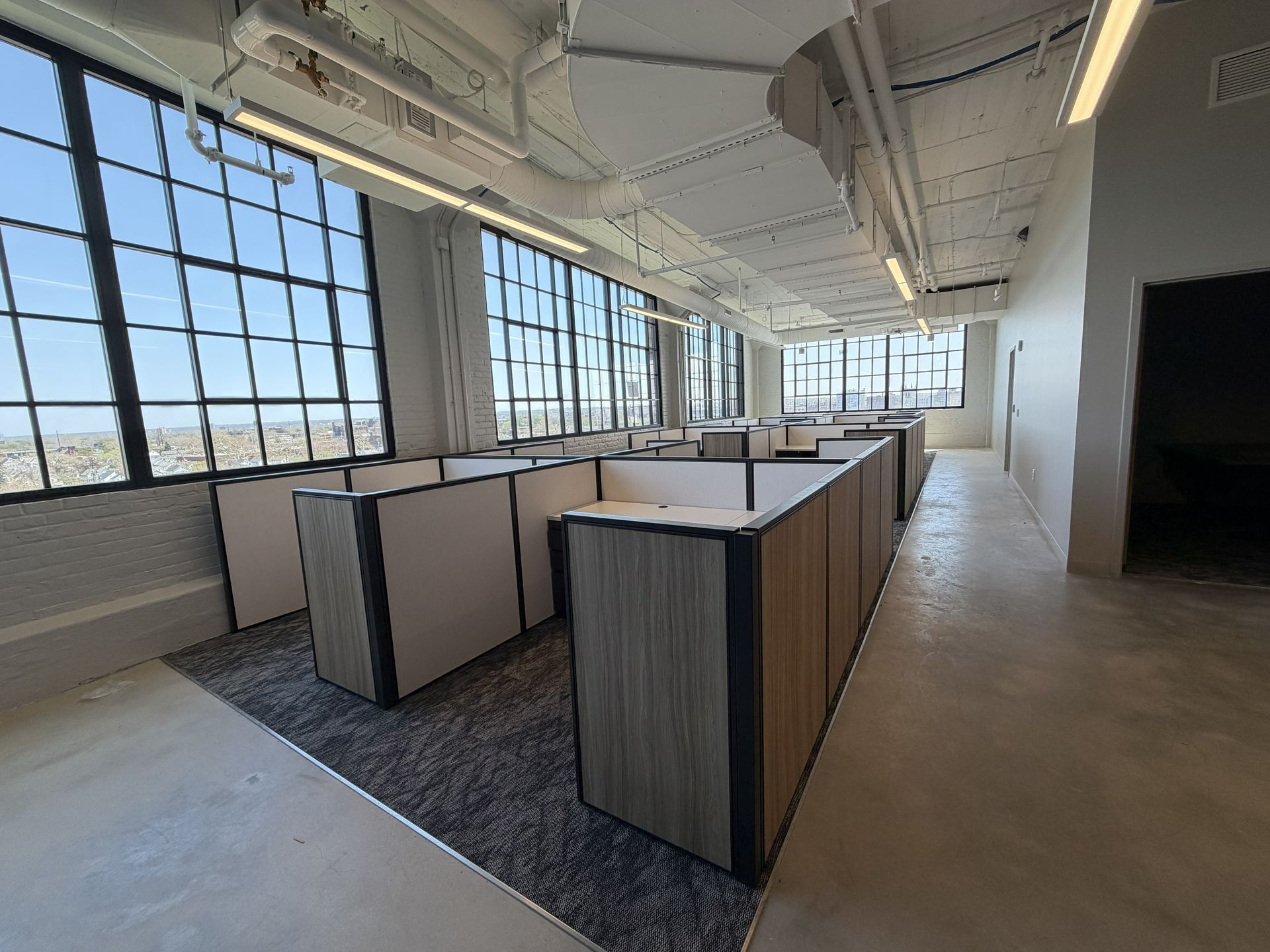 Empty modern open office with rows of cubicles, large windows, and exposed ceiling lights