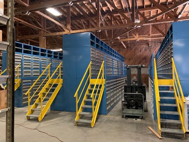 A warehouse with blue shelves and yellow stairs and a forklift.