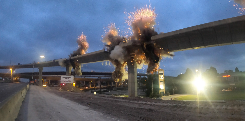 Smoke and sparks erupt from industrial structures at dusk beside a snowy road.