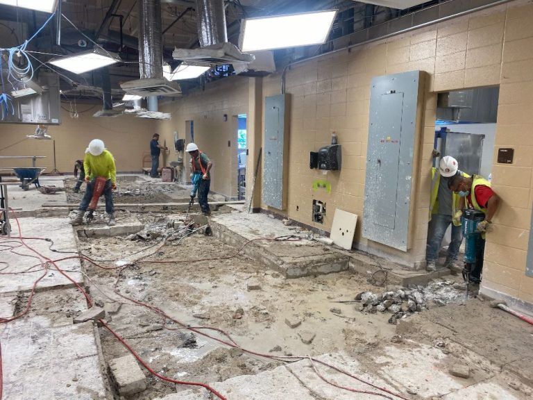 Construction workers demolishing an interior space with debris, tools, and exposed walls and ceiling.