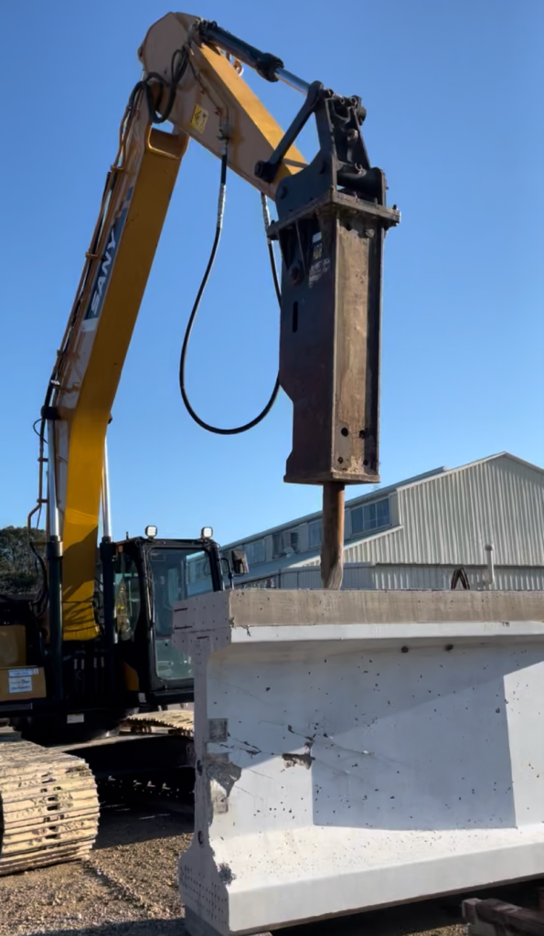 Yellow excavator with a hydraulic breaker demolishing a concrete structure at a construction site.