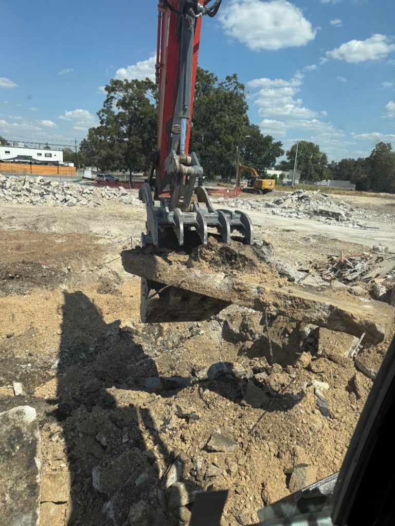 Excavator lifting a large concrete slab at a construction site under a clear blue sky