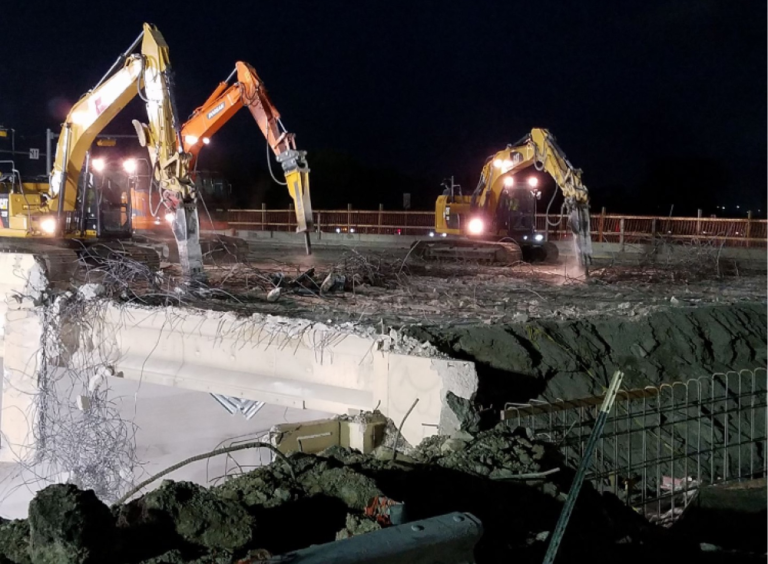 Two excavators working at night on a collapsed concrete structure at a construction site