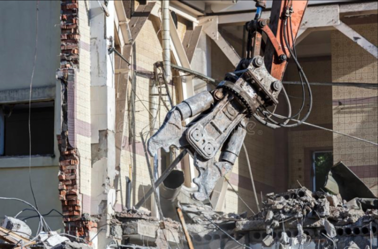 Rubble from a demolished building as an excavator arm tears through concrete and debris