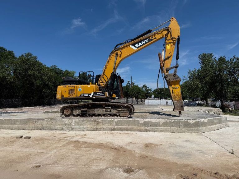Yellow excavator on a concrete pad at a construction site under a blue sky