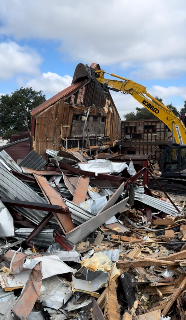 Demolition site with a yellow excavator tearing down a brick building amid rubble and debris