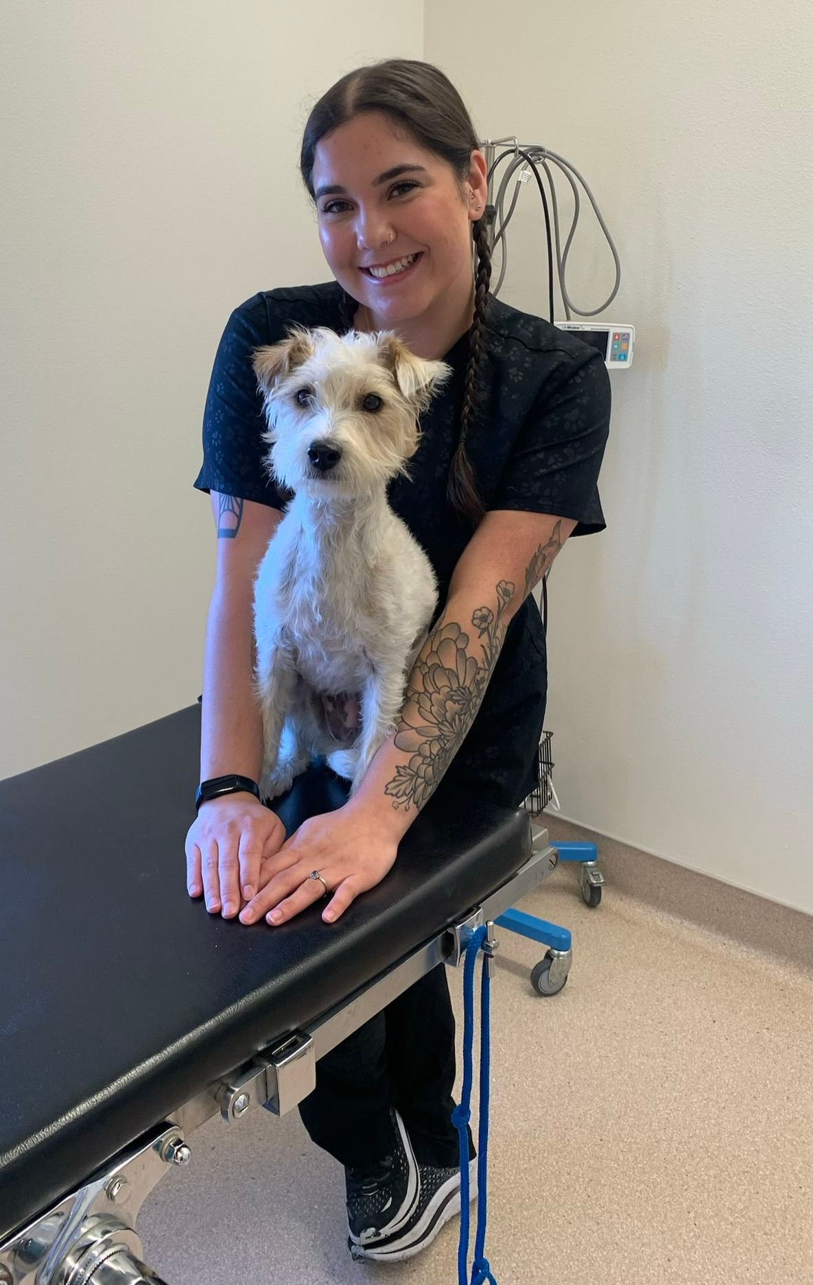 Veterinarian in blue scrubs smiling while hugging a golden retriever in a bright clinic