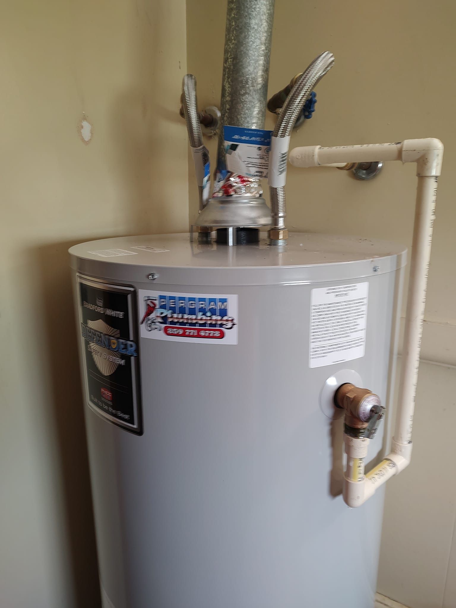 A cylindrical water heater with vent pipe and white PVC pipe attached, located in a room.