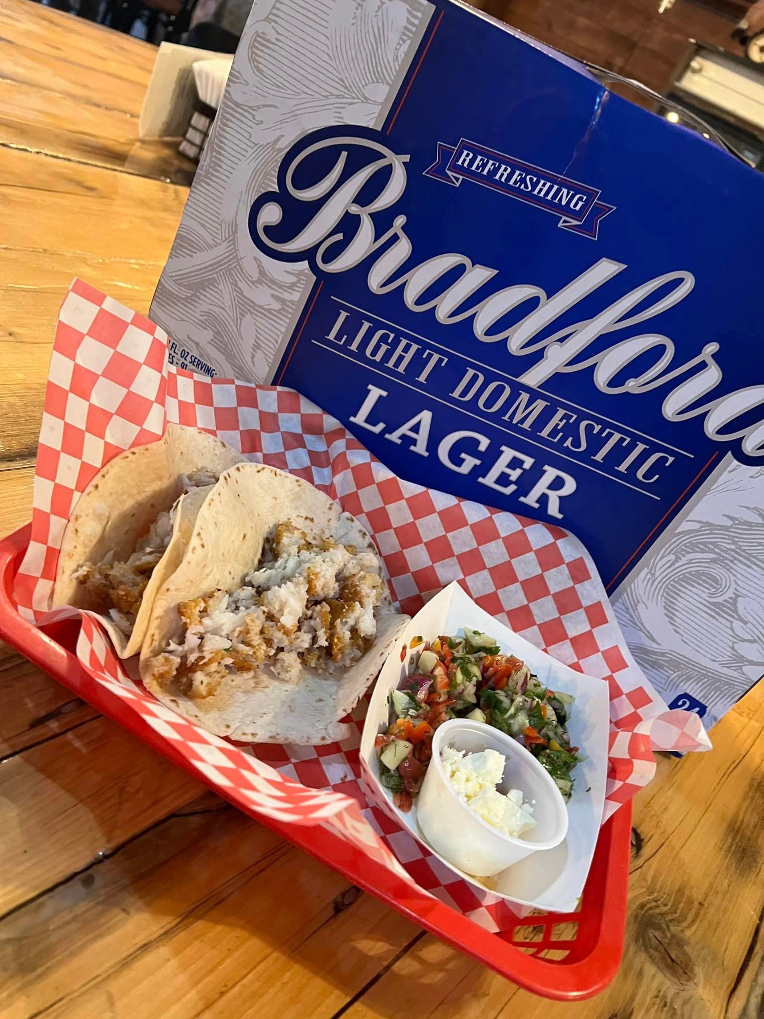 Case of Bradford Light Domestic Lager beside a couple fish tacos and pico de gallo from The Brewery kitchen.
