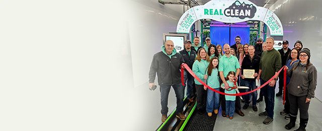 Group poses at a ribbon-cutting ceremony under a “Real Clean” sign.