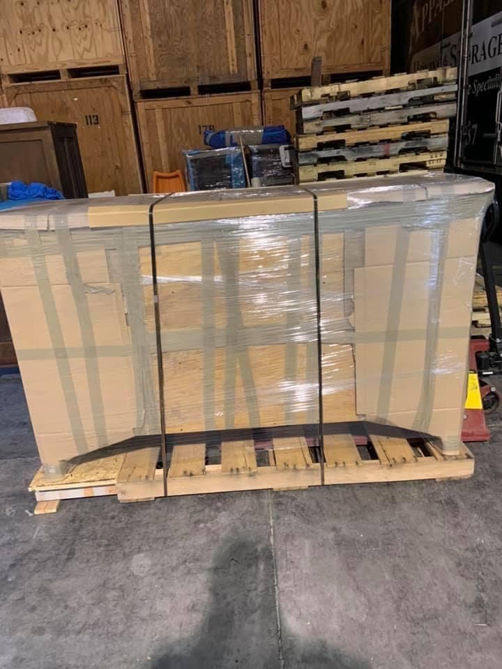 Palletized clear plastic panels strapped on a wooden pallet in a warehouse.